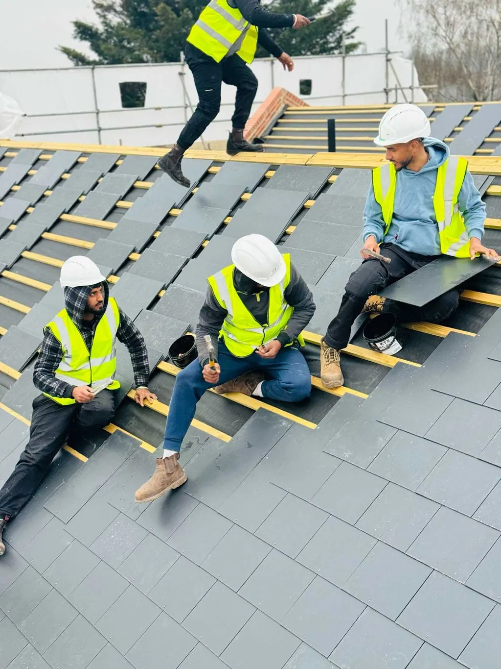 Roofers in high-visibility jackets laying grey slates