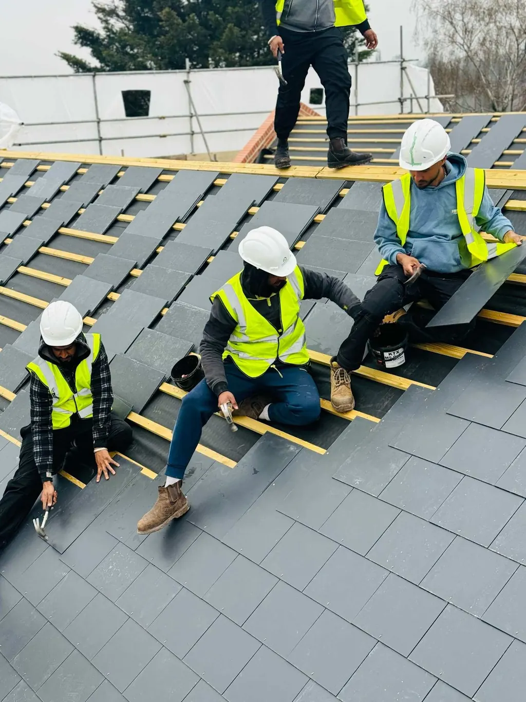 Roofers fixing slates across a partially covered roof